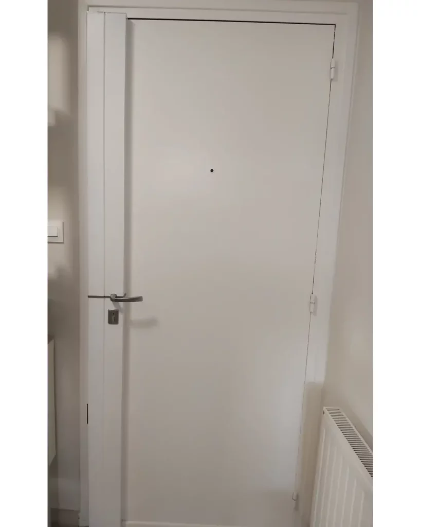 Porte d'entrée blanche équipée d'une serrure carénée multipoints, avec capotage vertical et poignée de sécurité.